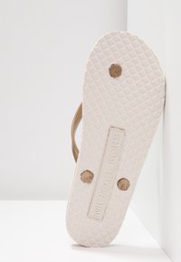 Michael Kors teenslippers, beige rubber bovenkant, witte textuurzool, logo detail op de voetbed, met twee kleine, ronde, gouden accenten.