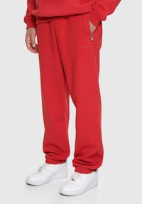 Rote Jogginghose mit lockerer Passform, elastischen Bündchen und seitlichem Reißverschlussfach. Hergestellt aus weichem Baumwollmix, kombiniert mit weißen Turnschuhen.