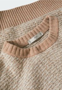 Beige gestrickter Pullover mit geripptem Kragen und Bündchen, Nahaufnahme der Textur und des MNG Man Kleidungslabels im Kragen.