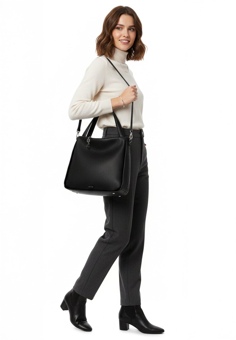 Woman in cream turtleneck, dark trousers, and black ankle boots carrying a large black leather handbag over her shoulder.