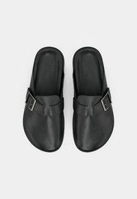 Μαύρα σανδάλια slip-on από λείο υλικό με ευρύ λουράκι και λεπτομέρεια με ασημένια αγκράφα, με απλή, σχηματισμένη σόλα για άνεση.