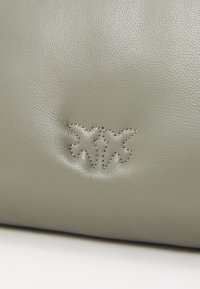 Groene leren tas met een gestructureerd oppervlak en een subtiel reliëflogo. De stiksels zijn licht, waardoor het logo-ontwerp wordt benadrukt.