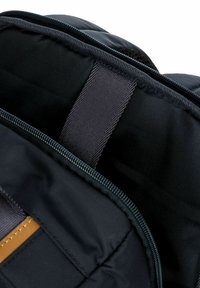 Interno di uno zaino nero in nylon con un compartimento imbottito e un accento in pelle marrone. Presenta una cerniera grigia e un rivestimento in tessuto testurizzato.