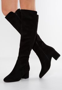 Bottes noires hautes jusqu'au-dessus du genou en daim. Bout carré et talon bloc, avec une fermeture éclair extérieure pour un enfilage facile. Texture lisse.