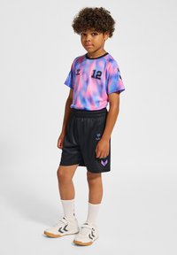 Färggad t-shirt med korta ärmar med rosa och blå virvlar, nummer 12, ihopparad med svarta shorts som har en logotyp och chevron-detaljer. Vita skor och strumpor.