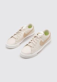 Zapatillas bajas de cuero beige con suela de goma blanca, diseño con cordones y acentos en logo dorado. Incluye forro interior verde.