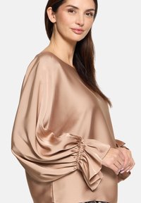 Silke bluse i nude, med lange, puffede ærmer med sammenkrøllede manchetter, glat tekstur og en afslappet pasform. Minimalistisk design med rund halsudskæring.