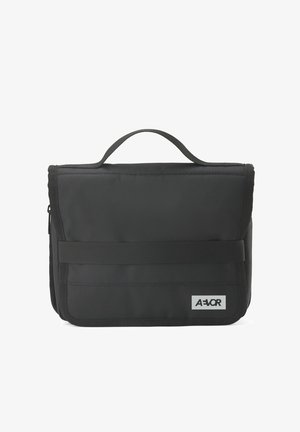 Schwarze rechteckige Tragetasche mit Griff, vorderem Riemen, Reißverschluss an der Seite und einem grauen AEVOR-Logo-Patch in der unteren rechten Ecke.