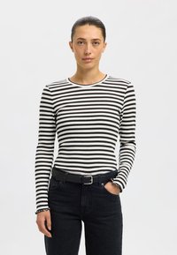 Hosszú ujjú fekete-fehér csíkos felső bordázott anyagból, kerek nyakkivágással és fodros mandzsettával, magas derekú fekete farmerrel párosítva.