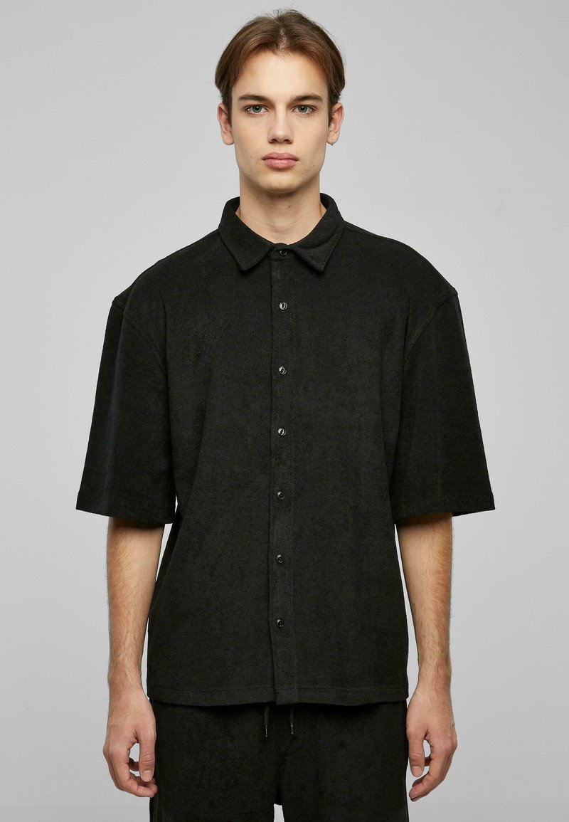 Camisa negra de manga corta y botones, con una textura suave, corte relajado y cuello apuntado. Presenta botones negros en la parte delantera.