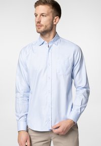 Jasnoniebieska, długa koszula zapinana na guziki z usztywnianym kołnierzykiem, jedną kieszenią na piersi i gładką fakturą materiału.