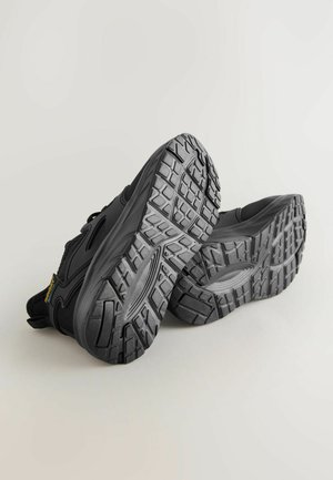 Baskets noires de sport avec des semelles en caoutchouc texturé, présentant un design épuré et un motif de bande de roulement pour une meilleure adhérence et traction.