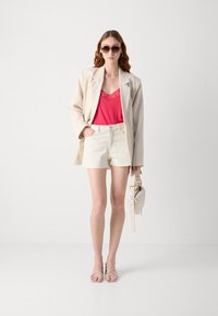 Beige linen oversized blazer over a pink lace-trimmed tank top, paired with white denim shorts, strappy sandals, and a light handbag.