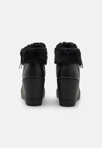 Botte à talon compensé en cuir noir avec un revers en fausse fourrure. Présente une finition lisse et des détails de couture discrets, offrant une silhouette arrondie et ajustée.