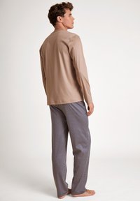 Beige lange mouw top gecombineerd met gestreepte marineblauwe pyjamabroek met kleine witte vormen. Zachte stof, ontspannen pasvorm, zichtbare stikseldetails.