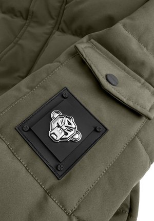 Olijfgroene pufferjack met een quiltontwerp; heeft een vierkante zwarte patch met een zilveren berenlogo en textuurdetails.