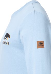 Ljusblå långärmad skjorta i mjukt tyg, med en svart björnlogo och en brun läderetikett med "FORSBERG" på ärmen.