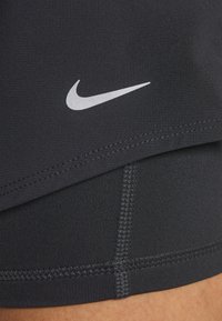 Zwarte sportshorts met een gladde textuur, voorzien van een zilveren Nike-logo en zichtbare stiksels langs de randen en de binnenvoering.