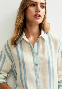 Camicia leggera button-up in crema con strisce verticali blu, colletto a punta e polsini con un bottone. Tessuto intrecciato con vestibilità rilassata.