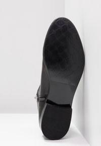 Semelle de chaussure habillée en cuir noir avec motif losange texturé, fermeture éclair latérale visible et petit talon empilé, sur fond blanc.