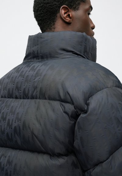 Jachetă tip puffer de culoare gri închis, cu finisaj mat. Prezintă un guler înalt, design matlasat și un model tonal subtil. Textură moale și umplută.