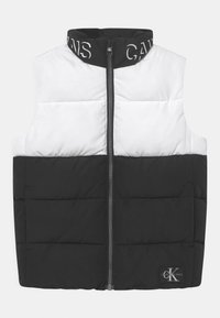 Prošívaná vesta s děleným designem; horní polovina bílá, dolní polovina černá. Má vysoký límec, přední zip a loga na límci a lemu.