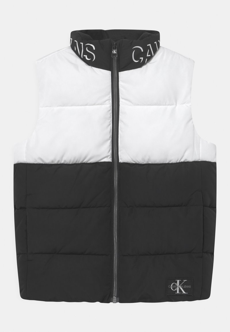 Prošívaná vesta s děleným designem; horní polovina bílá, dolní polovina černá. Má vysoký límec, přední zip a loga na límci a lemu.