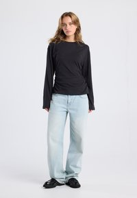 Black long-sleeve top with a fitted design, paired with light blue wide-leg jeans. Black chunky shoes complete the outfit.