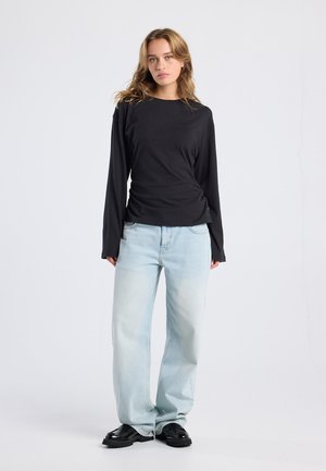 Zwarte lange mouwen top met een aansluitend ontwerp, gecombineerd met lichtblauwe wijde jeans. Zwarte chunky schoenen maken de outfit compleet.