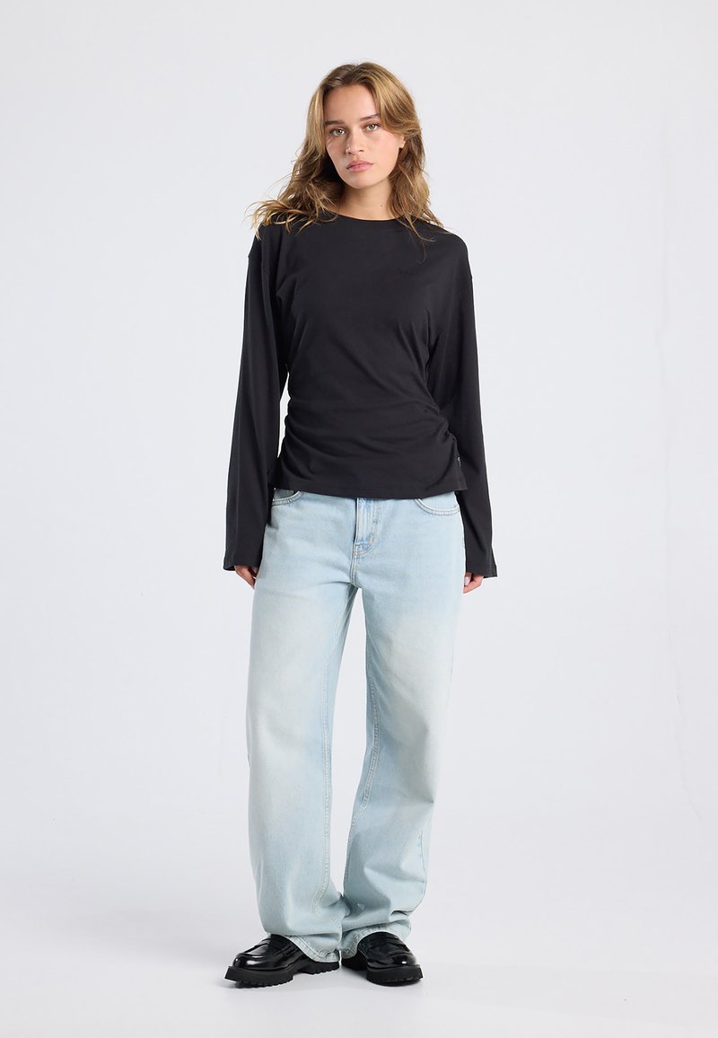 Black long-sleeve top with a fitted design, paired with light blue wide-leg jeans. Black chunky shoes complete the outfit.