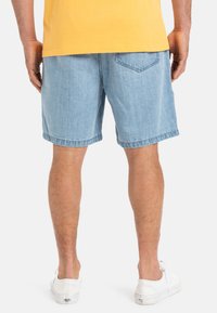 Lichtblauwe denim shorts met een relaxte pasvorm, twee achterzakken en een opgerolde zoom, gecombineerd met witte sneakers, getoond van de achterkant.