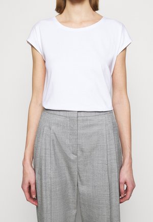 Mujer con una camiseta blanca de manga corta lisa metida en unos pantalones grises de corte tailored de tiro alto con pliegues delanteros.