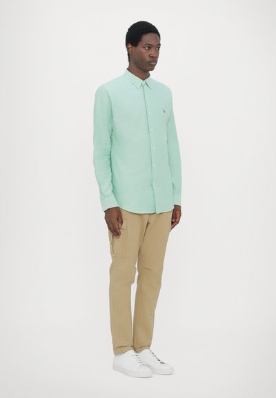 Chemise boutonnière mint, à manches longues et col, portée avec un pantalon cargo beige et des baskets blanches. Conception simple sans motifs.