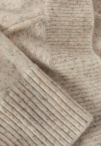 Beige kötött pulóver narancs és kék foltokkal. Bordás mandzsettákkal és olyan textúrával rendelkezik, ami puhán és melegen hat.