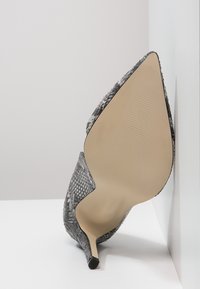 Spetsig tå högklackad sko i grå slangskinn, med en slät sula och texturerad ovandel. Smal design med stilettklack.