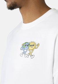 White cotton t-shirt featuring a printed graphic of a smiling sun and Earth character, both with exaggerated facial features and limbs.