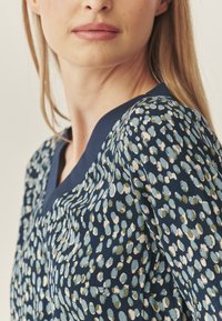 Bluză din țesătură multicoloră cu o bază bleumarin și modele de puncte în verde și albastru deschis. Decupaj în formă de V și material moale, texturat.