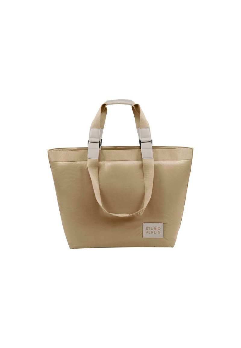 Beige tote bag med slitesterkt stoff, doble korte håndtak og kontrastfarget metall. Har en liten logo på den ene siden. Rektangulær form.