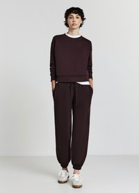 Dunkelbrauner, verkürzter Sweatshirt mit geripptem Saum, kombiniert mit passenden Jogginghosen mit Kordelzug. Weiße Sneakers runden das Outfit ab.