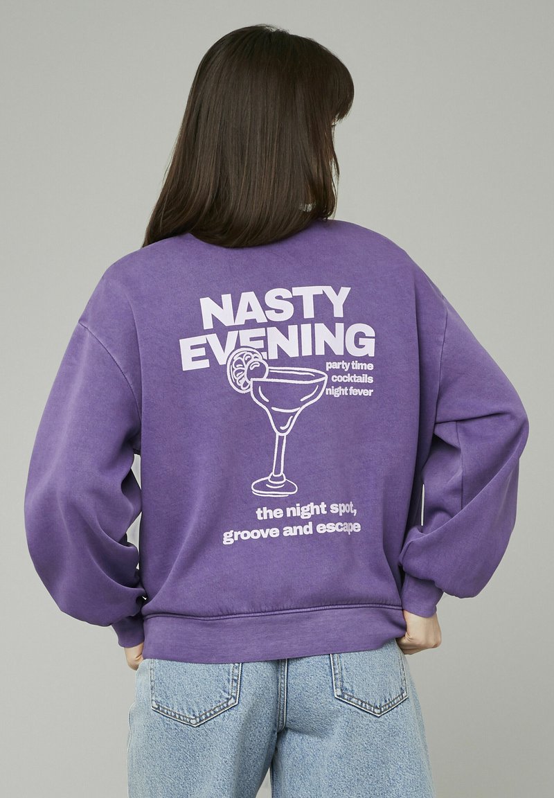 Sweatshirt violet à coupe oversize, avec un graphique blanc d'un verre à cocktail et le texte "NASTY EVENING" imprimé au dos.