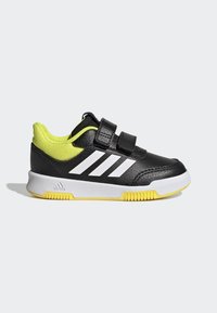 Zapatilla deportiva negra con rayas blancas, malla de nylon en amarillo y dos correas de velcro. Presenta una media suela blanca y una suela exterior amarilla.