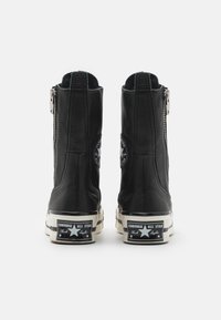 Sorte lær høye støvler med glidelås på siden, polstret krage og hvite gummisåler som har en klassisk Converse-logo på hælen.
