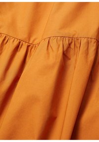 Tessuto di cotone arancione con dettagli arricciati lungo la cucitura, che mettono in risalto la texture e i motivi delle pieghe su tutto il materiale.