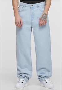 Heledad halli sinised teksad, mis on valmistatud denimist, klassikalise viie tasku kujundusega ja nööbike closure'iga, koos valgete tennisetossudega.