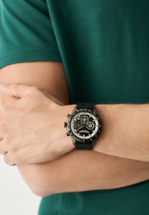 Must kronograafiga käekell tekstureeritud kummirihmaga ja valgete kontrastsete detailidega, millel on ümmargune sihverplaat mitme erineva ketta ja indikaatoritega.