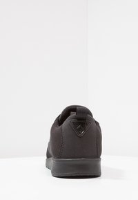 Sneaker Lacoste noire vue de l'arrière avec un tissu tricoté et une semelle en caoutchouc, affichant un écusson avec un logo triangulaire sur l'onglet du talon.