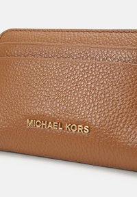 Smeđi kožni novčanik s teksturom i zlatnim logotipom "MICHAEL KORS". Ima više mjesta za kartice i glatku završnu obradu.