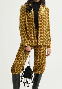 Abito in velluto giallo con motivo a fiori. Giacca su misura e pantaloni larghi con design floreale retrò. Gli accessori includono una pochette nera.