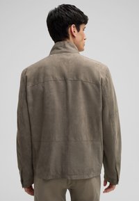 Suède jack in lichtgrijs, met een hoge kraag, lange mouwen en een eenvoudig ontwerp met minimale stiksels en zonder zichtbare hardware.