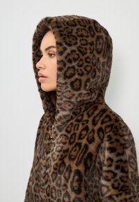 Manteau à capuche en fausse fourrure imprimé léopard ; présente un tissu doux et texturé avec des motifs bruns et noirs, mettant en valeur la taille généreuse de la capuche.
